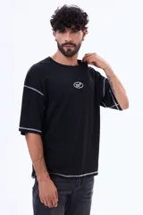 Remera negra de corte boxy con costuras a la vista en color blanco. Presenta un pequeño logo bordado en el centro del pecho y mangas cortas amplias.