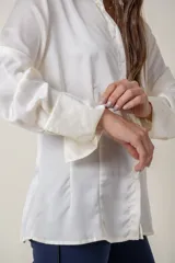 Camisa de seda con acabado satinado, de corte holgado y manga larga con puños anchos. Presenta cuello clásico y cierre frontal con botones al tono.