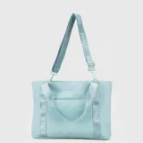 Tote bag de diseño funcional en color turquesa, con correas de hombro fijas y correa larga ajustable extraíble, ambas con el logo de la marca estampado. Cuenta con un bolsillo frontal abierto, compartimento principal con cierre y diseño resistente al agua.