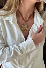 Collar con dije de bronce en forma de herradura con incrustación de nácar, montado sobre un cordón de cuero marrón.