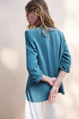 Blazer negro de cuello con solapas de muesca y hombreras, con mangas tres cuartos drapeadas, bolsillos de vivo simulados y cierre frontal con un botón dorado. Forro interior a tono.