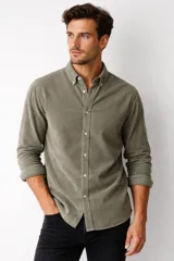 Camisa de pana color marrón, de manga larga, con cuello clásico abotonado y cierre frontal con botones.