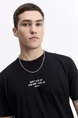 Remera de manga corta color beige con cuello redondo y estampado grande en la espalda. El estampado incluye un gráfico abstracto en tonos naranjas y morados, la palabra "Persistence" en vertical y un texto motivacional debajo.