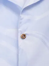 Camisa celeste con estampado de remolinos blancos, de corte recto, manga corta y cuello cubano.