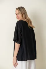 Blusa negra de viscosa con mangas cortas y detalle de broderie en los puños. Tiene cuello redondo y cierre frontal con botones.