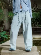 Pantalón de jean celeste lavado, de corte ancho y tiro alto con cordón ajustable en la cintura. Presenta detalles deshilachados en los bajos.