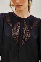 Camisa de color azul marino con mangas tres cuartos abullonadas y puños elásticos. Presenta un diseño con paneles de encaje negro en el frente y cuello redondo.