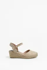 Sandalia de plataforma con cuña de yute y suela texturizada, color beige. Cuenta con puntera cerrada, diseño destalonado y tira ajustable al tobillo con hebilla metálica.