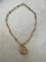 Collar largo de cuentas de piedras semipreciosas en tonos tierra, con dijes de conchas marinas.