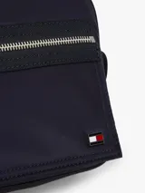 Morral cruzado Tommy Hilfiger de diseño práctico y funcional, confeccionado en poliamida reciclada azul marino con forro de poliéster. Cuenta con un compartimento principal, bolsillo exterior con cierre de cremallera, correa ajustable extraíble y detalles distintivos con la bandera metalizada de la marca.