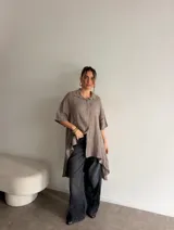 Camisola de lino color marrón topo, de corte oversize, con mangas cortas, cuello camisero clásico y cierre frontal de botones. Presenta un diseño asimétrico con el ruedo más largo en la parte trasera.