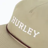 Gorra tipo trucker de color beige con visera curva y cordón marrón oscuro en la unión de la copa y la visera. Presenta la palabra "HURLEY" bordada en blanco en el panel frontal.