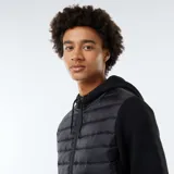 Buzo negro con capucha, cierre frontal con cremallera y mangas largas. El cuerpo es acolchado y las mangas son de tejido liso.