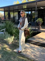 Chaleco tejido de punto en color chocolate, con cuello redondo y diseño sin mangas. Presenta un aplique frontal decorativo compuesto por tres figuras en forma de rombo en tonos tierra, bordeadas con hilo crudo.