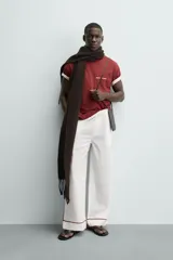 Camiseta blanca de corte relajado (relaxed fit) con cuello redondo y manga corta. Presenta un bolsillo plastrón en el pecho y un estampado de texto en color marrón rojizo en la espalda que dice "SOMETIMES SÍ, SOMETIMES BYE" (reemplazando la 'O' de 'SOMETIMES' por un corazón).