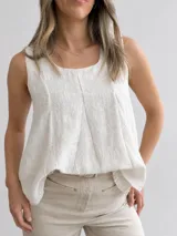Blusa blanca sin mangas, con escote redondo y diseño evasé de doble capa con textura sutil en relieve.