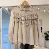 Camisa beige de manga larga con cuello camisero, cierre frontal de botones y detalles de volados con bordado broderie en el frente.