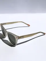 Lentes de sol Osten modelo Porto con armazón de acetato en tono beige traslúcido y acabado mate. Presentan detalles en color naranja en el frente y en las patillas, con el logo de la marca grabado en el lateral.
