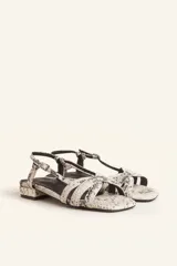 Sandalias bajas con estampado de piel de serpiente en tonos blanco y negro. Tiras finas entrecruzadas en el empeine, pulsera al tobillo con hebilla ajustable y pequeño tacón cuadrado.