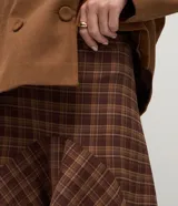 Pollera midi de sastrería con estampa de cuadros en tonos marrones. Posee diseño mullet, más corta al frente y alargada atrás, cintura alta y recortes que aportan movimiento.