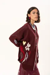 Saco de punto color vino con diseño holgado, cuello redondo y mangas largas. Presenta un gran bordado central en la espalda con forma de flor en tonos crema y rojo, acompañado de un pequeño bordado de sol y una frase bordada en la parte inferior.