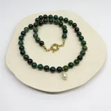 Collar de cuentas de ágata musgo de 8 mm con nudos de hilo verde entre cada piedra. Presenta un dije central de perla barroca con herrajes bañados en oro.