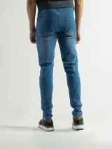 Jean negro de corte slim fit, tiro medio, con cierre y botón. Presenta un ligero desgaste en la zona de los muslos.