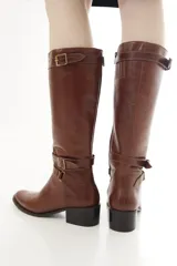 Bota de caña alta de cuero liso negro, con diseño clásico, detalles de hebillas metálicas, cierre lateral y taco bajo.