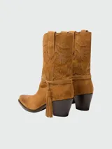 Botas estilo western de gamuza color tostado, con diseño de caña media y bordados decorativos en forma de flores. Presentan un detalle de cordón con borlas en el tobillo y taco cuadrado.