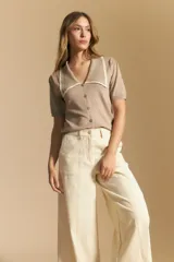 Top de tejido color beige claro, manga corta, escote en V con cierre frontal de botones y ribetes negros en el cuello y el borde del escote.