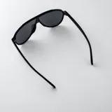 Lentes de sol con armazón de policarbonato negro y diseño de estilo aviador con puente superior plano. Las lentes son de color amarillo y cuentan con filtro UV400. Las patillas incorporan detalles metálicos dorados en las bisagras.