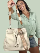 Bolso tipo bucket color crema, confeccionado en cuero texturizado. Tiene doble asa de mano y correa bandolera desmontable con apliques de cuero marrón y beige.