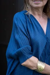 Vestido largo azul marino con escote en V, mangas anchas y textura plisada. Presenta capas de flecos que caen desde el pecho hasta el ruedo.