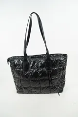 Cartera tipo shopper de color negro, con diseño acolchado y costuras cuadradas. Cuenta con doble asa larga para llevar al hombro y cierre superior.