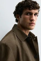 Sobrecamisa de corte relajado confeccionada en piel con acabado de ante. Presenta cuello solapa, cierre frontal con botones, mangas largas con puños abotonados y dos bolsillos delanteros de plastrón.