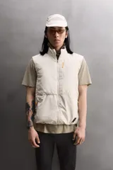 Chaleco técnico de corte regular con cuello subido y cierre frontal de cremallera. Presenta un diseño ligero con panel frontal ligeramente acolchado, bolsillos laterales con cremallera oculta y un bolsillo adicional en el pecho con tirador en color naranja. Incluye acabados con cinta elástica en el bajo y detalle de logo estampado.