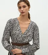 Vestido midi de tejido satinado con estampado abstracto, escote en V, mangas largas con volumen y hombreras estructuradas. Incluye un cinturón con hebilla para marcar la cintura y falda fluida con recortes.