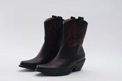 Botas de estilo western (texanas) de caña media, color blanco, confeccionadas en cuero. Presentan bordados decorativos en la caña y puntera cuadrada. Cuentan con cierre lateral y taco de altura media.