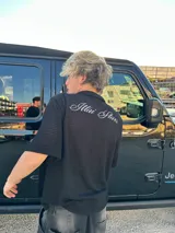 Camisa negra de manga corta con cuello, confeccionada en tejido texturizado (tipo waffle o piqué). Presenta un bordado en la espalda con el texto "Ittai Stars" en hilo blanco.