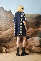 Vestido corto de punto jacquard color azul marino, con diseño de estrellas blancas alineadas verticalmente en los laterales. Presenta cuello polo con cierre frontal de botones y mangas cortas con detalles de rayas en contraste.