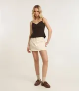 Short pollera de sarga color beige, con diseño de tiro medio, trabillas en la cintura, bolsillos laterales y cierre frontal con botón y cremallera.