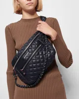 Riñonera negra capitoneada con tres cierres frontales, correa ajustable con hebilla y cadena metálica decorativa.