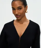 Cardigan de punto negro con escote en V, cierre frontal mediante ganchos metálicos y mangas largas con puños ajustados. Presenta un diseño entallado en la cintura con mangas ligeramente abullonadas.