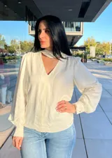 Blusa de satén color off-white, con cuello tipo choker, escote en V y mangas largas abullonadas con puños ajustados.