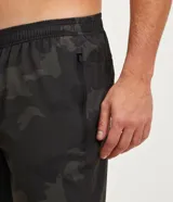 Bermuda deportiva de poliéster con estampado camuflado en tonos grises y blancos, cintura elástica con cordón ajustable y bolsillos laterales con cierre.