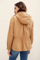 Campera estilo militar color tostado, confeccionada en 100% algodón, con cuello alto, cierre frontal de cremallera, bolsillos con solapa en el pecho y cordón ajustable en la cintura.