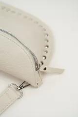 Cartera tipo riñonera o bandolera de cuero sintético negro con textura granulada, forma de media luna y detalles de tachas plateadas en el borde inferior. Cuenta con cierre metálico plateado y correa ajustable.