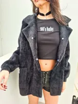 Saco negro de textura peluda con cuello de piel sintética desmontable, cierre frontal con botones y dos bolsillos delanteros.