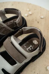 Sandalias de cuero marrón con diseño de tiras anchas y ajuste mediante velcro. Presentan una plantilla acolchada color tostado con detalles en rojo y una suela de goma negra con plataforma dentada.