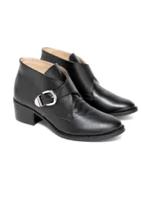 Bota corta de cuero vacuno grabado con terminación charolada, color negro. Presenta un diseño de solapa cruzada con cierre de hebilla metálica plateada y taco medio fachetado con efecto madera.